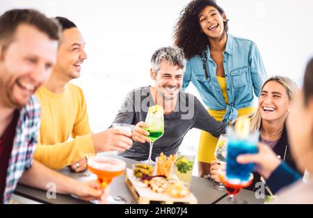 Amici che tostano drink colorati alla terrazza del cocktail bar all'aperto - concetto di stile di vita con i giovani che si divertono insieme a condividere cocktail Foto Stock