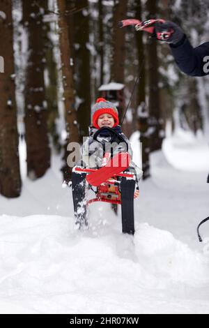 un ragazzo felice in discesa su una slitta in inverno, un bambino in abiti luminosi siede su una slitta, la neve lo vola Foto Stock