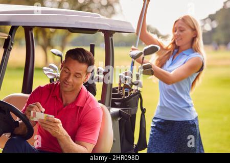 Coppia che gioca Round on Golf insieme seduto in Buggy con Score Card e Choosing Clubs Foto Stock