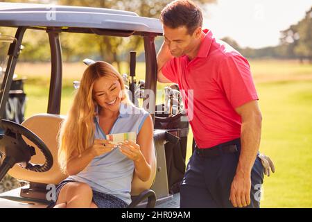 Coppia seduta in Buggy giocando Round on Golf e Checking Score Card insieme Foto Stock