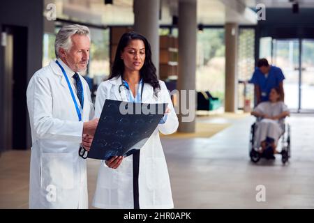 Due medici in camici bianchi e discutere la scansione del paziente in ospedale occupato Foto Stock