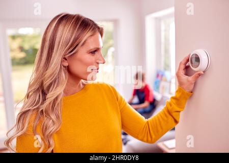 Madre a casa con Son Adjusting Smart Central Heating Thermostat Control Foto Stock