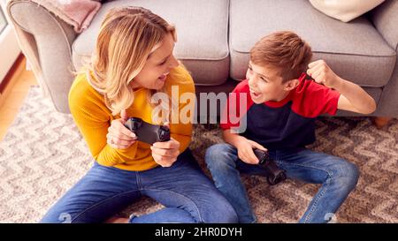Madre e Figlio a casa giocando il videogioco insieme a ragazzo che celebra quando vince Foto Stock