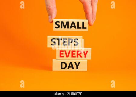 Simbolo piccoli passi ogni giorno. Parole di concetto piccoli passi ogni giorno su blocchi di legno. Mano dell'uomo d'affari. Bella tabella arancione sfondo arancione. Piccola Foto Stock
