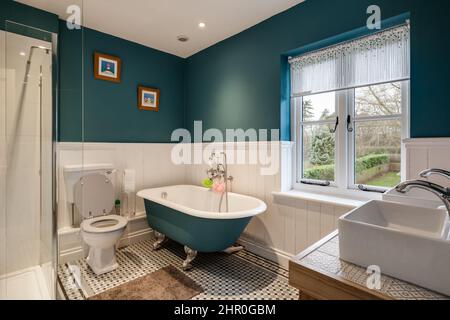 Cavendish, Suffolk - Jan 19 2019: Bel bagno in stile vittoriano con vasca da bagno in ghisa con bordo a rullo, pareti blu pavone e bianche, piastrelle a mosaico st Foto Stock