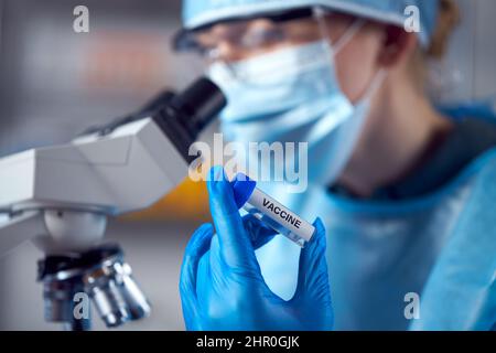 Primo piano di un lavoratore di laboratorio femminile che indossa PPE cercando vaccino con microscopio Foto Stock