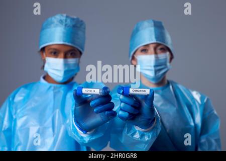 Due addetti alla ricerca di laboratorio di sesso femminile in provette di fissaggio PPE etichettate Covid-19 e Omicron Foto Stock
