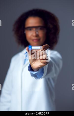 Medico femminile o lavoratore di laboratorio che indossa PPE e occhiali di sicurezza che tiene il flacone o la provetta Foto Stock