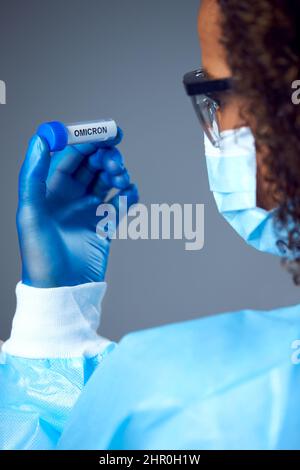 Lavoratore di ricerca di laboratorio femminile che indossa la provetta di prova di tenuta PPE etichettata Omicron Foto Stock