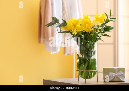 Vaso con fiori gialli e regalo sul tavolo in camera Foto Stock