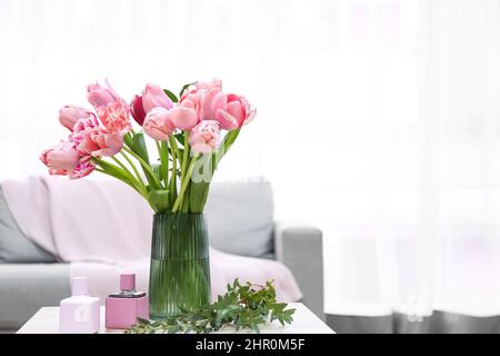 Vaso con tulipani rosa, bottiglie di profumo e rami di piante sul tavolo in soggiorno