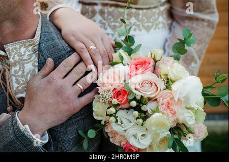 Anelli di nozze d'oro, le mani della sposa e lo sposo su un bouquet di fiori Foto Stock