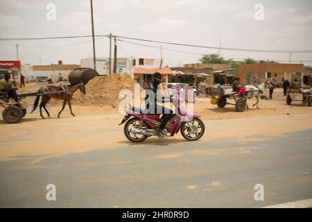 Carretti trainati da cavalli e motociclette condividono la strada attraverso una piccola città nel nord del Senegal, Africa occidentale. Foto Stock