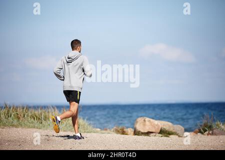 Corsa verso il fitness. Scatto retroguarato di un giovane che corre sulla spiaggia. Foto Stock