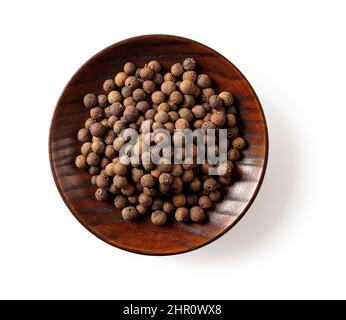 Bacche di pimento di allspizia su un piatto di legno marrone isolato su sfondo bianco. Grani di pepe della Giamaica su una pentola per cucinare. Concetto di spezia organica. Foto Stock