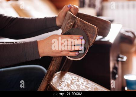 Primo piano di signora rimuovendo vecchio strato di vernice e levigare la superficie dello sgabello con carta vetrata in casa officina. Pratiche sostenibili. Riutilizzo di cose vecchie Foto Stock