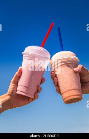 I milkshake tenuti in mano sullo sfondo del cielo blu in giornata di sole. Foto Stock