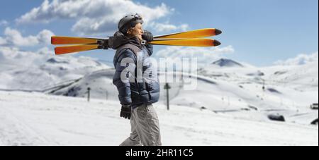 Uomo maturo in una giacca invernale che cammina e trasporta gli sci su una montagna innevata Foto Stock