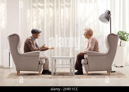 Uomo e donna anziana seduti in poltrone e conversando a casa in soggiorno Foto Stock