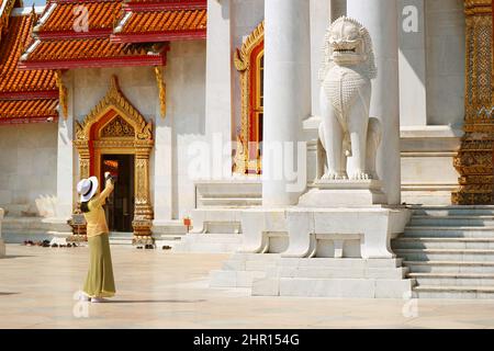 Visitatore femminile che prende foto del Leone Guardiano all'ingresso della Sala d'ordinazione di Wat Benchamabophit (il Tempio di marmo) a Bangkok, Thailandia Foto Stock