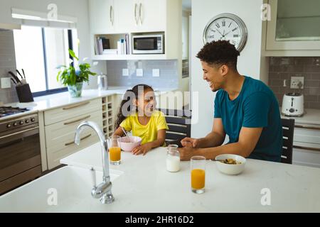 Buon padre e figlia biraciale che si guardano l'un l'altro mentre si gusta la colazione insieme Foto Stock