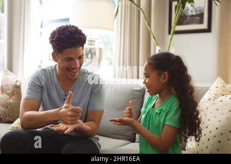 Felice padre e figlia biraciale comunicare attraverso il linguaggio dei segni a casa Foto Stock