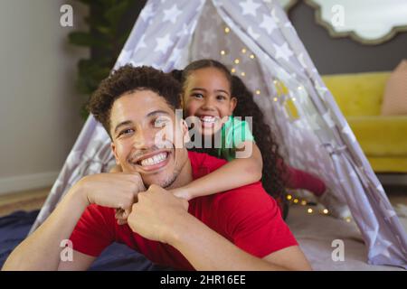 Ritratto di sorridente figlia biraciale e padre giacente in tenda a casa Foto Stock