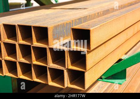 profilo quadrato in metallo in una pila, tubi metallici di sezione quadrata sul sito di un negozio di materiali da costruzione, materiali da costruzione in metallo, profil arrugginito Foto Stock