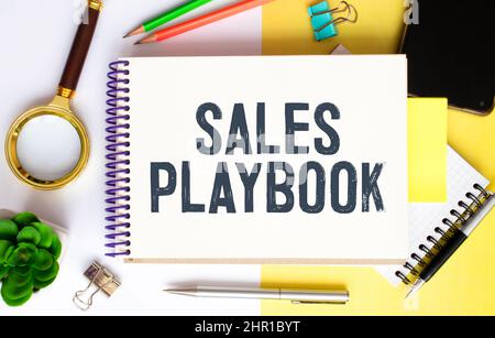 playbook di vendita su blocco note con penna, occhiali e calcolatrice. Foto Stock