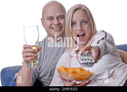 La coppia gode di una serata accogliente guardando la TV con una ciotola di patatine e un bicchiere di birra Foto Stock