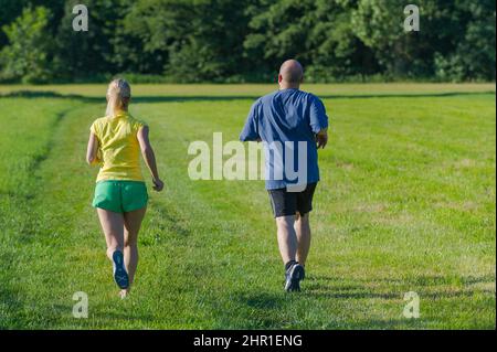 coppia jogging insieme attraverso un prato, vista posteriore Foto Stock