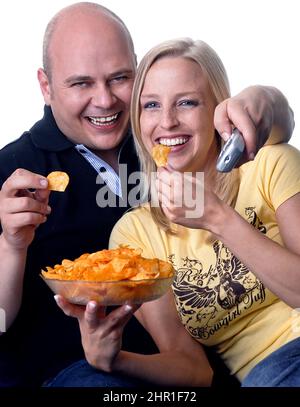 La coppia gode di una serata accogliente guardando la TV con una ciotola di patatine Foto Stock