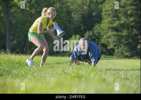 la donna sportiva rallegra il suo marito non sportivo per allenarsi con un megafono Foto Stock