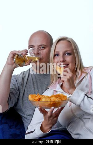 La coppia gode di una serata accogliente guardando la TV con una ciotola di patatine e un bicchiere di birra Foto Stock