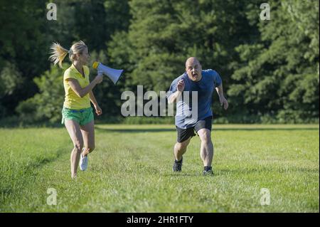 la donna sportiva rallegra il suo marito non sportivo per allenarsi con un megafono Foto Stock
