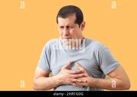 Colpo di un uomo che tiene il suo petto in disagio a causa di dolore con sfondo giallo.concetto di attacco di cuore. Foto Stock