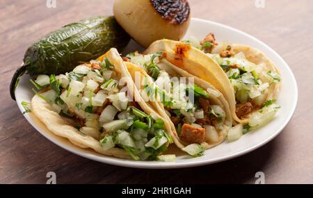 Tre Tacos di strada di pollo piccante in una fila su un tavolo di legno Foto Stock