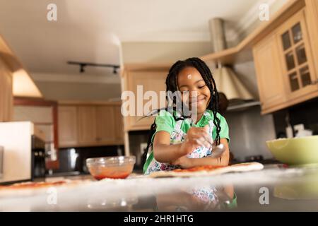 Sorridente ragazza afroamericana carina con trecce nere che fanno la pizza al banco della cucina Foto Stock