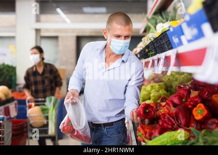 Uomo in maschera scelta del peperone rosso in gregrocer Foto Stock