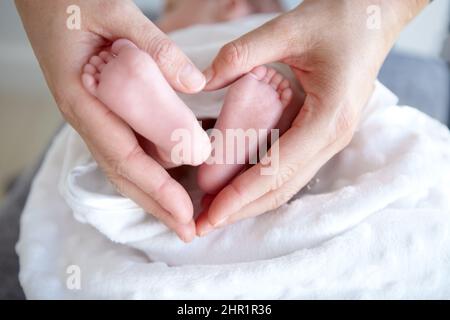 Amore più puro. Una madre che tiene le sue ragazze del bambino i piedi piccoli nelle sue mani in modo che formi un cuore. Foto Stock