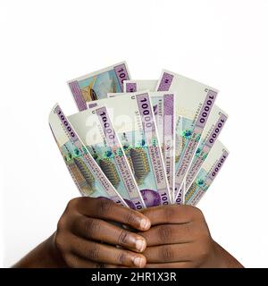 Le mani nere che detengono 3D hanno reso 10000 banconote del franco di CFA dell'Africa centrale. Primo piano delle mani che tengono le banconote della valuta nigeriana Foto Stock
