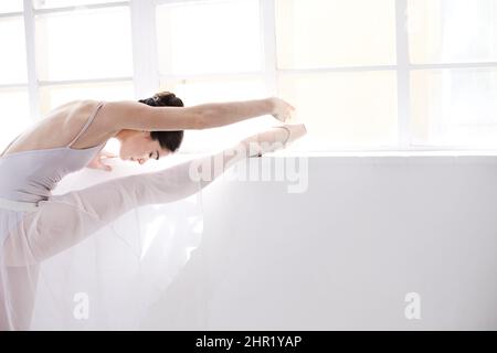 Grazia in movimento. Giovane ballerina flessibile che si allunga a fianco di un muro bianco. Foto Stock