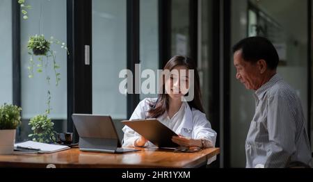 Donna asiatica medico mano tenendo penna e parlare con il paziente anziano circa il farmaco e il trattamento Foto Stock