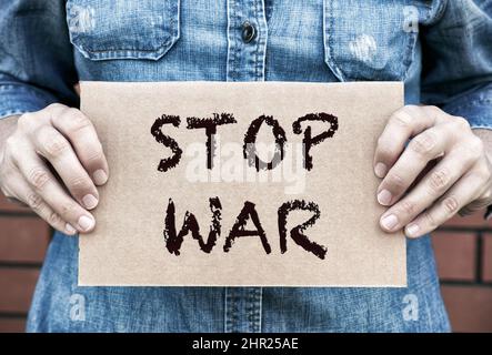 Donna mani che tengono pezzo di cartone con le parole Stop War contro mattone parete sfondo. Foto Stock