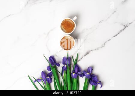 Due tazze di caffè caldo del mattino a forma di numero 8 e bouquet di iridi violetti su sfondo marmoreo. Disposizione piatta con spazio di copia per il testo. Biglietto di auguri per la Festa della Donna e il 8th marzo. Foto Stock