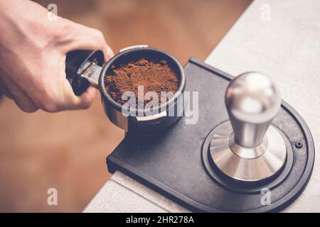 Barista che tiene in mano il portafiltro con caffè fresco preparare il caffè press con manomissione. Primo piano Foto Stock