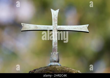 croce di metallo su una lapide di un cimitero di fronte a sfondo verde sfocato Foto Stock