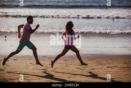 Giovane uomo e donna che corrono a jogging lungo il mare. Coppia che corre sulla spiaggia. Foto Stock