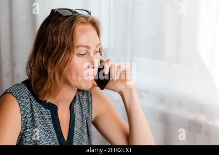 Lavoro a distanza. La donna lavora a casa al computer e parla al telefono. Il concetto di quarantena, di freelance e di autoisolamento. Foto Stock