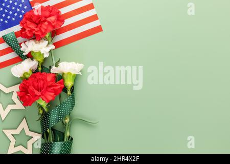 Composizione per le festività americane con bouquet di garofani e bandiera americana su sfondo verde con spazio per la copia adatto per il Memorial Day, 4th luglio Foto Stock